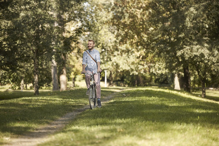 one young man, 20-29 years, riding bicycle in park trail outdoors. looking sideways, enjoying happy.の写真素材