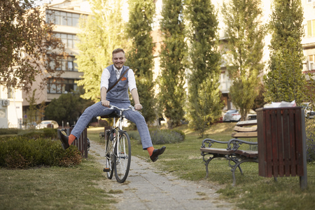 one young man, 20-29 years old,  wearing hipster suit, smart casual, ridiculous funny riding bike (legs spread) in park road trail.の写真素材