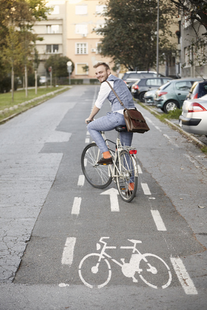 one young man, 20-29 years old,  wearing hipster suit, smart casual, looking back to camera, rear view. in city on bike track (bicycle sign painted on asphalt).の写真素材