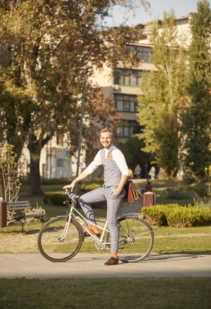 one young man, 20-29 years old, wearing hipster suit, sitting posing on a old retro city bike outdoors, on sunny day, in park.の写真素材