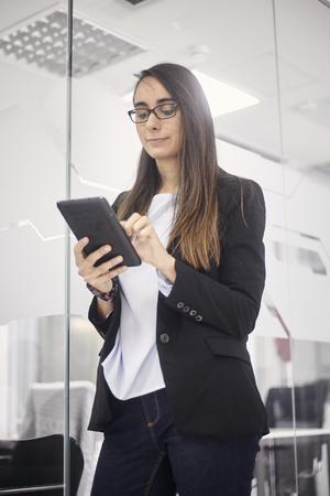 one young woman portrait, 20-29 years old, standing, modern office space indoors, using tablet. low angle view.の写真素材
