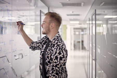 one young man, writing on glass window wall of modern office ideas, with marker.の写真素材