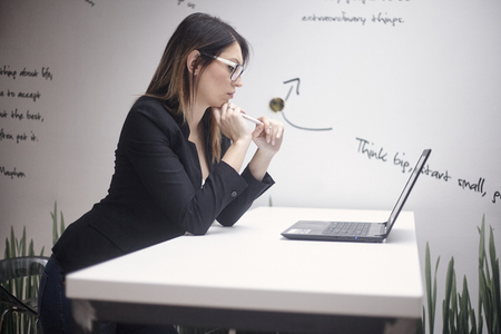 one young woman thinking, 30-39 years old, side view, upper body shot. working on laptop. wall with creative quotes  behind.の写真素材