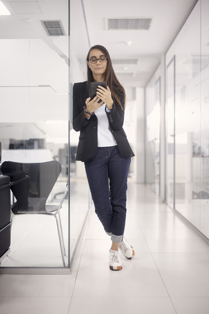 one young woman standing, 20-29 years, smart casual clothes, using tablet in modern interior office. full length shot.の写真素材