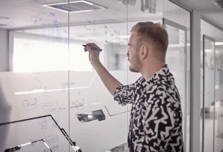 one young man, writing on glass window wall of modern office, with marker.の写真素材