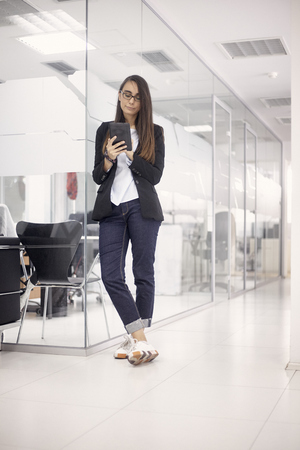one young woman, white collar worker, standing enjoying her work, using tablet. full lenght shot, in modern interior office space.の写真素材