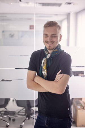 one young smiling man, 20-29 years old, casual clothing, arms crossed, standing leaning on glass...