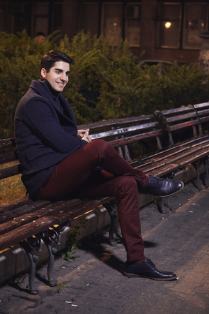one handsome young man, 20-29 years old, posing, autumn clothes, sitting bench on city square. night time, dark.の写真素材