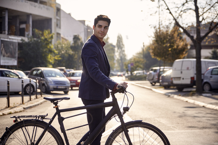 one young handsome smiling man crossing street, pushing bicycle outdoors, busy street cars (out of focus in background).の写真素材