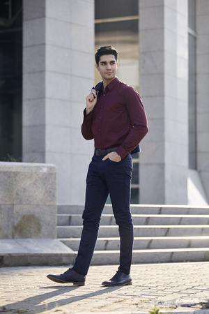 one young handsome man smirking, looking sideways, wearing suit, casually walking on pavement. modern building out of focus behind.の写真素材