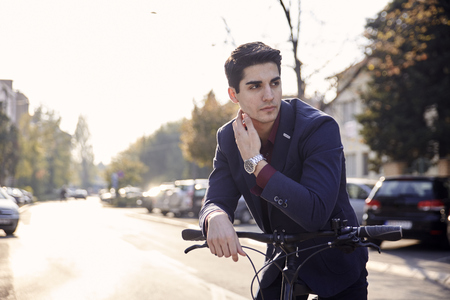 city street cars (out of focus in background), one young man posing in foreground, looking sideways, bicycle handlebar outdoors. 20-29 years old, wearing suit.の写真素材
