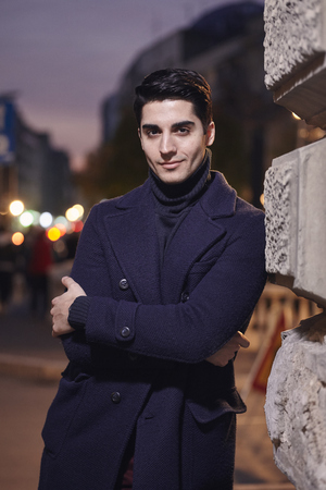night time sunset, one young man, 20-29 years old, leaning on wall on street building, looking to camera. wearing Autumn clothes.の写真素材
