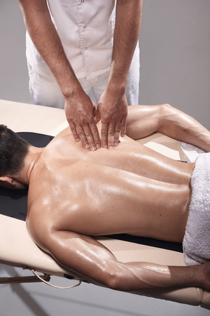 two young man, 20-29 years old, sports physiotherapy indoors in studio, photo shoot. Physiotherapist massaging patient back with his hands.の写真素材