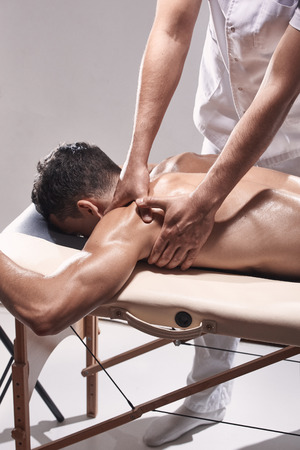 side view, two young man, 20-29 years old, sports physiotherapy indoors in studio, photo shoot. Physiotherapist massaging patient shoulder with his hands.の写真素材
