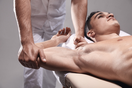 two young man, 20-29 years old, sports physiotherapy indoors in studio, photo shoot. Physiotherapist massaging muscular patient back with his hands.の写真素材