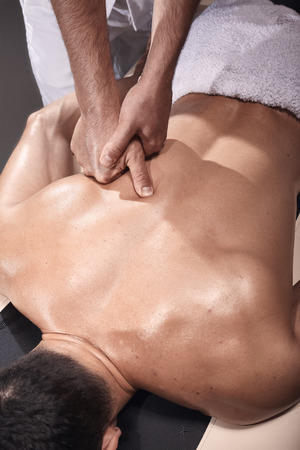 two young man, 20-29 years old, sports physiotherapy indoors in studio, photo shoot. Physiotherapist massaging muscular patient back with his one hand close-up.の写真素材