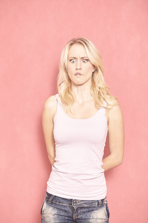 one young woman, funny expression while her lips are sealed, she is looking down at them. 20-29 years old, long blond hair. Shot in studio on pink background.の写真素材