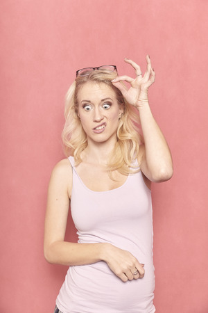 one young woman, 20-29 years old, long blond hair. Shot in studio on pink background. weird face expression, eyes wide open.の写真素材