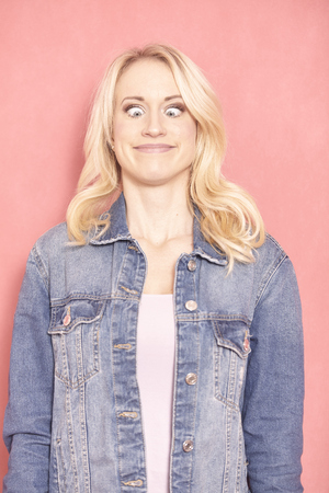 one young woman, 20-29 years old, long blond hair. Shot in studio on pink background. looking down, eyes wide open, face expression acting like a frog.の写真素材