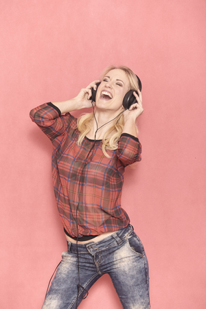 one young woman, hilarious laughing emotion, shouting while listening to music on headphones. 20-29 years old, long blond hair. Shot in studio on pink background.の写真素材