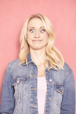 one young woman, 20-29 years old, long blond hair. Shot in studio on pink background. looking down, eyes wide open, face expression acting like a frog.の写真素材