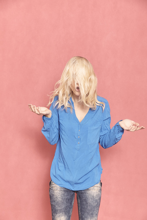 one young woman, 20-29 years old, messy chaotic long blond hair, almost hilarious since her face can't be seen, arm's raised in doubt. Shot in studio on pink background.の写真素材