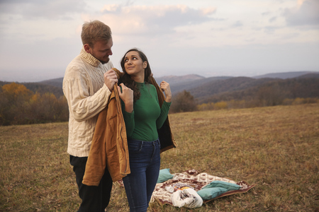 two people, young couple, 20-29 years, lovely gesture gentleman putting his jacket on woman's back, standing behind her. picnic outdoors on mountain field, in national park "Fruska Gora", Serbia.の写真素材