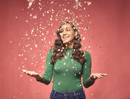 one young smiling woman, 20-29 years, confetti falling down, while her arms are outs outstretched. she is looking friendly and welcoming. shot in studio on pink background.の写真素材