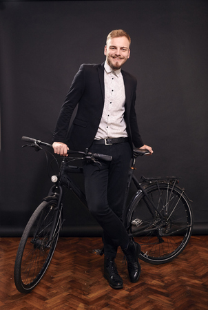 one young man smiling honestly, 20-29 years old, posing, leaning on on a bicycle inside studio. black seamless background behind him. real person, not a model.の写真素材