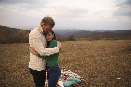 two young people, couple hugging outdoors in mountains field, on a picnic vacation.の写真素材