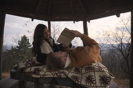 two people, young couple or friends, laying on desk (in summer house) relaxing and enjoying. Woman listening while man is reading the book, together. In national park "Fruska Gora", Serbia.の写真素材
