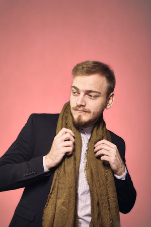 one young gentleman, 20-29 years old, posing with suit and scarf, looking sideways. pink background, studio shot, photo shoot.の写真素材