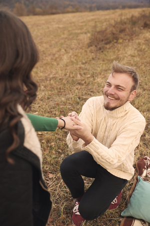 Young smiling happy man kneeling proposing to young woman, 20-29 years old, alone on mountain field. Autumn.の写真素材
