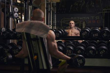 one man, 30-39 years, looking at himself in mirror, training at home gym holding dumbbells.の写真素材