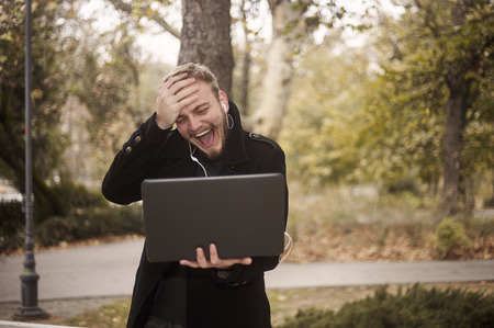 one young laughing man, can't believe it, while he is candidly gesturing putting his palm on his forehead. holding laptop in hand, communicating over Internet video call, could be family.の写真素材