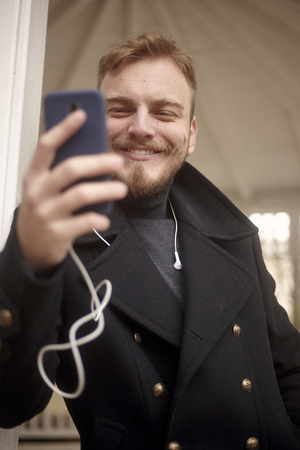 low angle shot of one young smiling man, 20-29 years old, texting and using his smart-phone.の写真素材