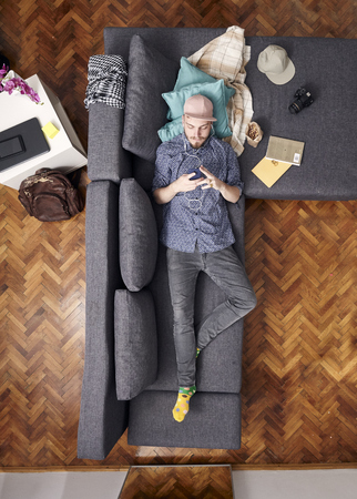 one young hipster, laying in couch in his room. using smartphone. bird's eye view; view from above.の写真素材