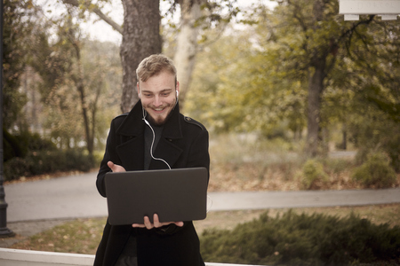one young smiling and happy man, holding laptop in hand, communicating with someone (gesturing with one hand) over video call, could be communicating with family.の写真素材