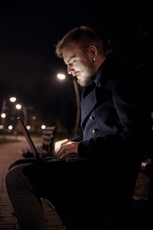 dark night, one young man, 20-29 years, sitting on bench alone, using his laptop in public park in Autumn.の写真素材