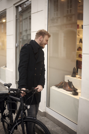 one young man, 20-29 years old, shopping for fancy shoes. standing in front of a store with his bicycle, looking to a window shop.の写真素材