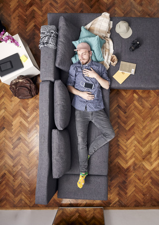 one young hipster man, laying in bed sleeping. whole sofa and bed visible, view from above.の写真素材