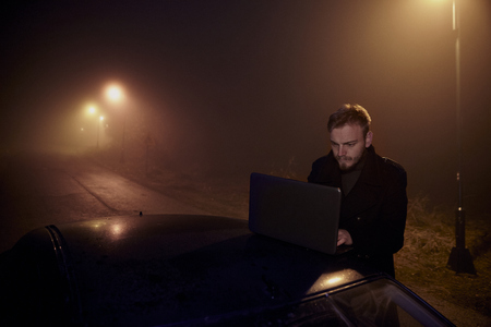 one young man, working (using) his laptop computer on a car roof, in dark night, rural area.の写真素材
