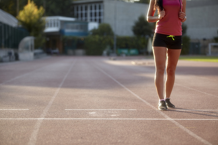 one young woman, unrecognizable person, wearing fitness clothes, walking on a sports court. On a track and field, running tracks.の写真素材