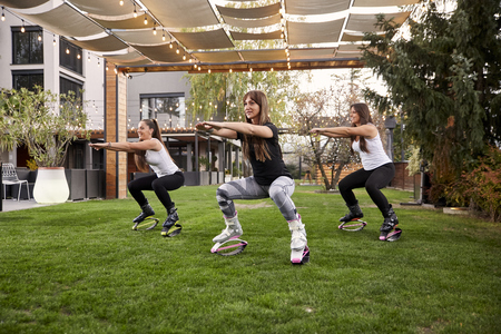 three young ladies,20-29 years old, doing squats in jump boots in a backyard of a a fancy house.の写真素材