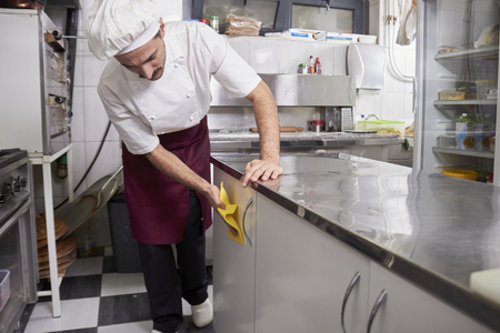 young chef in kitchen wiping cabinets, after closing restaurant.の写真素材