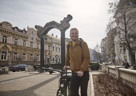 one young man, smiling and happy, holding and posing with his bicycle. standing in a old city square, in European old traditional style architecture.の写真素材