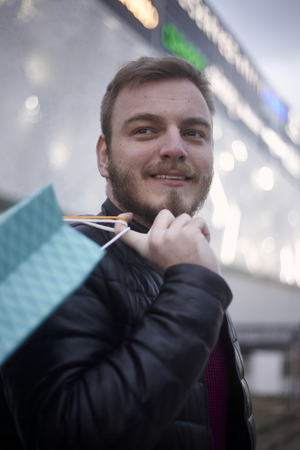 face, head portrait of young man holding shopping bags in front of a shopping mall outdoors. looking sideways.の写真素材