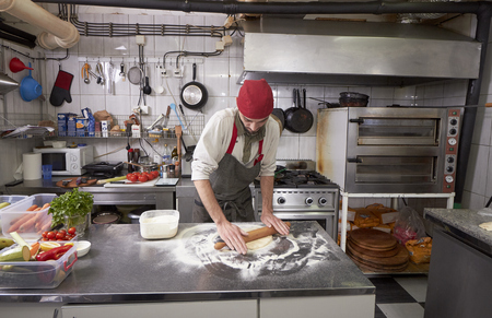 One young chef,20-29 years old, making dough for pizza indoors in a commercial kitchen.の写真素材