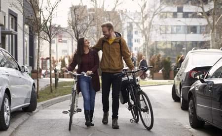 two friends or couple, 20-29 years, walking and talking on a street, pushing their bicycles, looking at each other.の写真素材