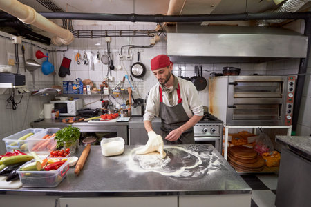 One young chef, 20-29 years old, making a pizza dough in a commercial kitchen.